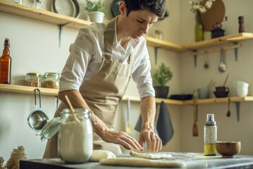 A baker in an apron kneads the dough with his hands and sprinkles it with flour to bake delicious homemade bread.