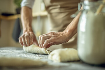 A baker in an apron kneads the dough with his hands and sprinkles it with flour to bake delicious homemade bread.