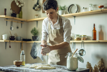 A baker in an apron kneads the dough with his hands and sprinkles it with flour to bake delicious homemade bread.