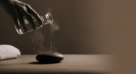 Hand pouring essential oil onto smooth hot stone with rising steam on neutral background. Aromatic therapy. Spa. Wellness, massage services, aromatherapy, relaxation retreats, stress management