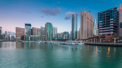 Fototapeta premium Dubai Marina towers and yachts reflected in water of canal in Dubai day to night timelapse