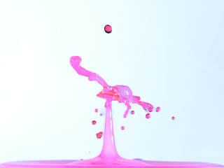 A vibrant pink water splash with a dark red droplet colliding at its peak, captured mid-air against...