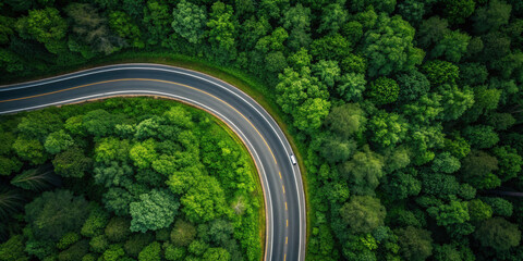 Curved highway surrounded by dense green forest captured from drone view, showing single vehicle on road with vibrant natural scenery and peaceful atmosphere