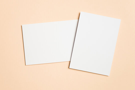 Two blank white cards arranged overlapping on a beige surface, one vertical and one horizontal, ideal for showcasing wedding invitations or elegant stationery.