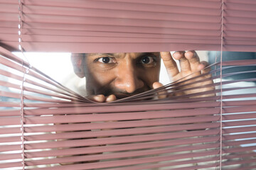 Nosy businessman peeking through venetian blinds in office