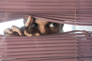 Curious businessman looking through venetian blinds spying on someone