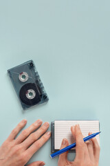 Young woman writing playlist of retro songs from 80s. Close-up of an empty audio cassette with a blank playlist list, showcasing potential for custom song recordings