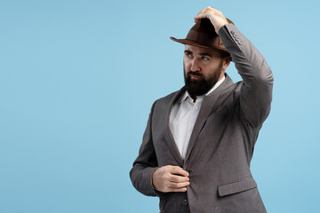 Elegant businessman adjusting his hat and suit on blue background