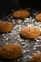 Craft and rustic four oatmeal cookies. Dark food aesthetics, black background with several oat flakes.