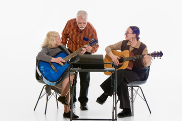Two senior women and man, pensioners learning guitar together around laptop, showing collaboration...
