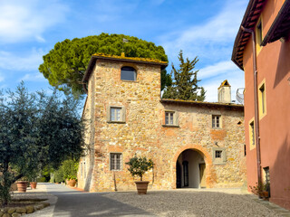 rustic Tuscan old stone house with arched entrance surrounded by lush green trees and terracotta buildings under a bright blue