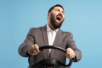 Stressed businessman screaming while driving with steering wheel on blue background