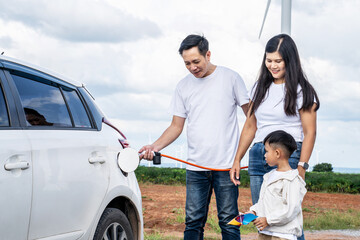 Asian family charging the ev car with eco-friendly, windmill in background, Electric vehicle driven...