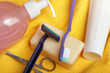 The personal hygiene set on yellow towel background. Shampoo, scissors, razor, soap and toothbrush for everyday care.