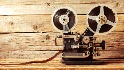 Obraz premium Vintage film projector on rustic wooden background with film reel