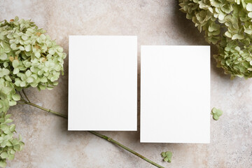 Double blank wedding invitation cards mockup on a neutral stone surface surrounded by pale green...
