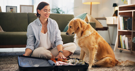 Suitcase, clothes and woman with dog in home packing for travel, holiday and international vacation. Animal, pet and happy person with Golden Retriever on floor with luggage to prepare for trip
