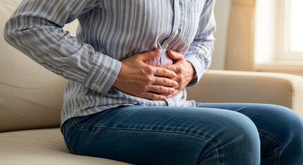 Woman Experiencing Abdominal Pain Gripping Stomach While Sitting on Sofa in Bright Light Living Room