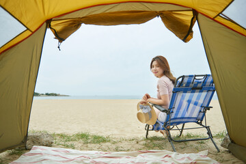 Young woman sitting on a beach chair inside a tent, relaxing and enjoying the ocean view