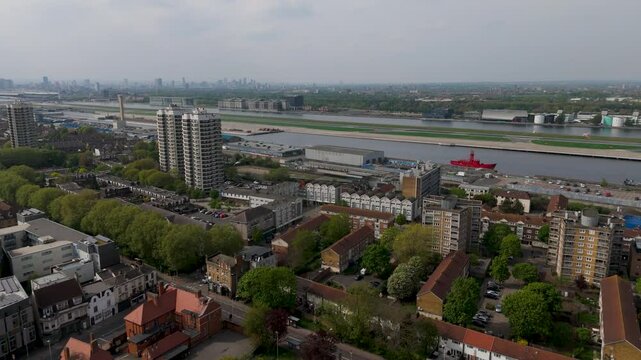 Drone Rising over Houses in front of London City Airport, DLR Train, Misty Skyline