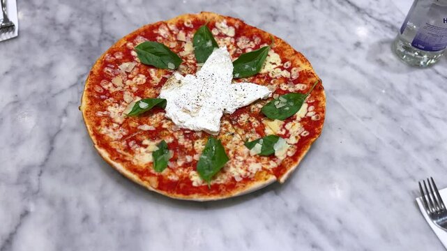 4K close-up of a freshly baked gourmet pizza topped with creamy burrata, basil, and shaved cheese on a marble surface&mdash;ideal for food ads, menus, and cooking videos.