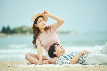 Young Woman and Man Relaxing Together on Beach, Woman Wearing Straw Hat