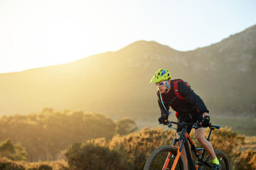 Man, mountain or sunset with bike for cycling, extreme sport or fitness on dirt track in nature. Active, male person or cyclist riding with helmet on off road or desert terrain in outdoor wilderness