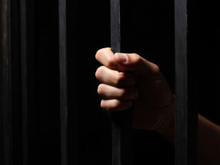 Despair: hand holding onto jail cell bars.
