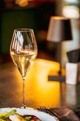 A close-up shot of a sparkling glass of white wine, reflecting warm light. The elegant ambiance is complemented by soft lighting, setting the mood for a refined dining experience.

