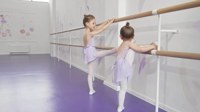 Two adorable little ballerinas stretching gracefully at ballet school