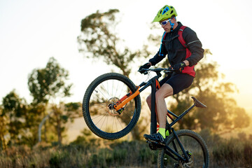 Fototapeta premium Balance, bike and jump with man in mountains for adrenaline, adventure or training off road. Exercise, fitness and wheelie trick with sports person cycling in nature for challenge or performance
