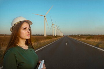 Close-up female engineer in hard hat holding plan on road, strong turbine perspective view.