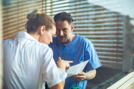 Doctors discussing urgent medical results through a glass window in hospital setting