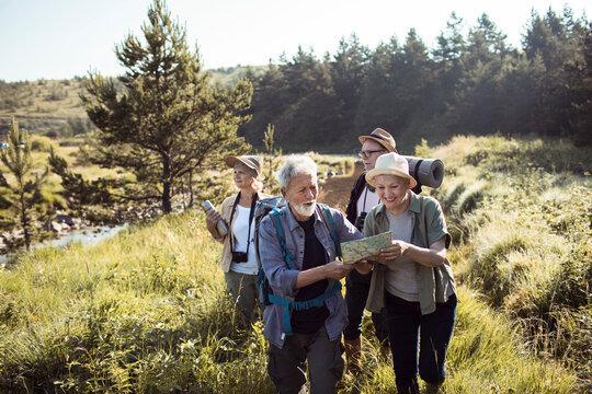 Group of senior hikers navigating forest trail with map near river