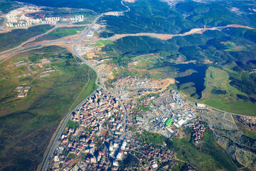 Aerial view of a small town in Turkey, with urban infrastructure. Dense buildings, highways, and road systems. Town surrounded by green hills. Water reservoir in the rural area. 