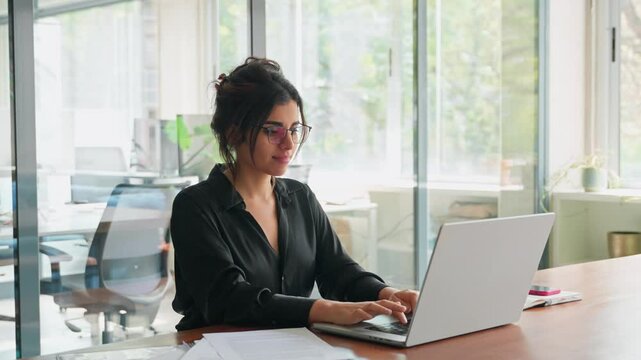 Focused latin hispanic young business woman working on laptop computer reading financial document report in office. Accountant entrepreneur manager businesswoman doing paperwork using pc. Copy space