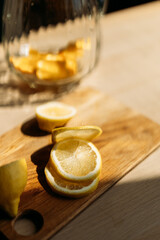 A clear glass pitcher filled with fresh lemon slices sits on a wooden surface, ready for homemade lemonade. Natural lighting highlights the concept of summer refreshment and organic ingredients.