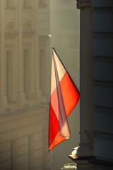 Biało-czerwona flaga Polski oświetlona wschodzącym słońcem na budynku podczas święta państwowego