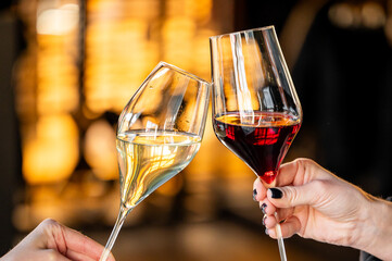 Two wine glasses are clinking in a celebratory toast, one filled with white wine and the other with red. The warm, blurred background adds a festive atmosphere to the moment.