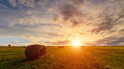 Scenic sunset over hay bales in a field. Golden light bathes the landscape, creating a tranquil scene. For agriculture, travel and inspiring greeting card designs.