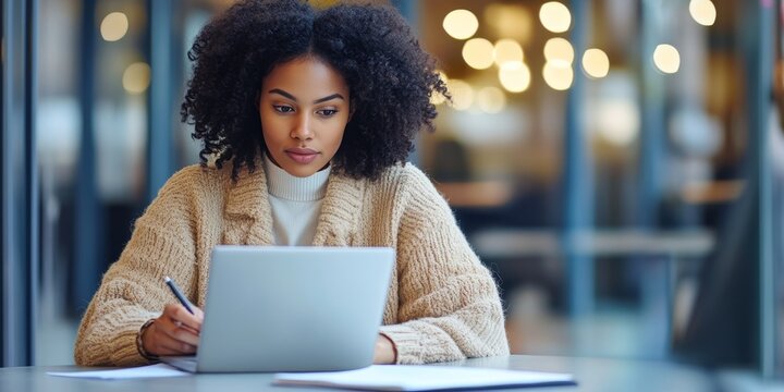 The image shows a professional woman in an office environment, deeply engaged in her work. She is focused on paperwork or computer documents, demonstrating attention to detail and productivity.