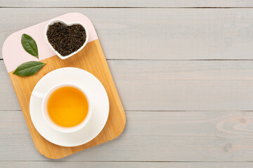 Cup of tea with dry and fresh leaves on wooden background, top view