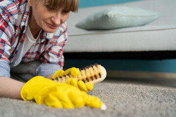 Cleaning concept. Middle-aged woman cleans carpet with hard brush in room