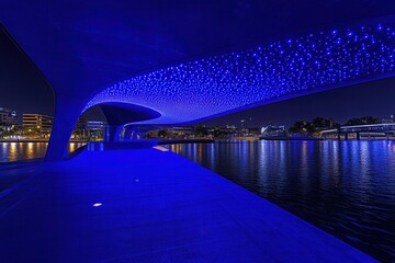 Night view of a modern illuminated bridge over a river with city skyline in the background