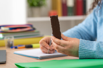 Student hand holding chocolate snack bar studying at home.