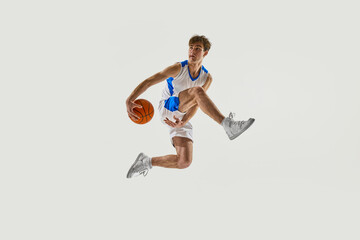 Basketball athlete floating mid-air, legs spread with control, executing high jump with ball...