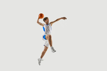 Explosive basketball jump by athlete with ball clutched against white studio background, showing power and energy in moment of goal. Concept of sport, competition, active and healthy lifestyle, game © Lustre Art Group 