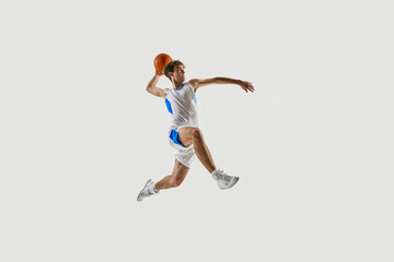Dynamic photo. Young basketball player mid-jump, leaning forward with focus and grip on ball in...