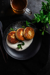 Cheesecakes with cream sauce and mint in a black plate on the table. Breakfast