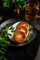 Cheesecakes with cream sauce and mint in a black plate on the table. Breakfast